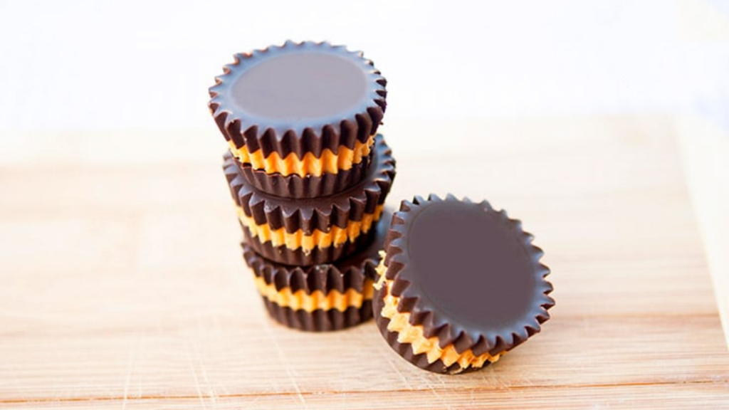 Three stacked peanut butter cups with a forth resting on the side, all sit on a wood surface.