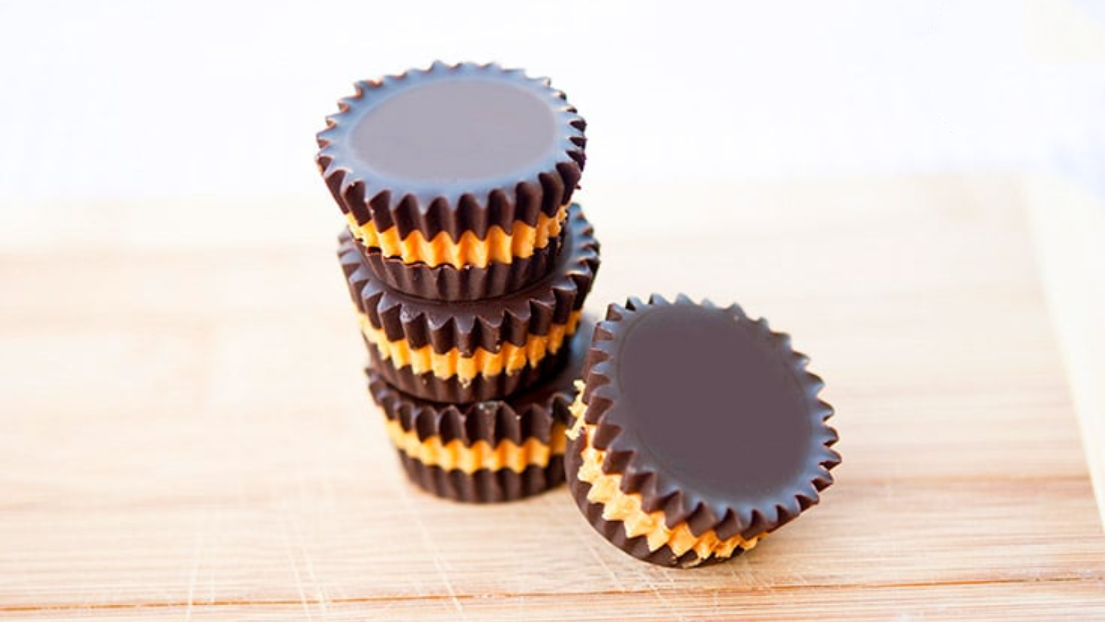 Three stacked peanut butter cups with a forth resting on the side, all sit on a wood surface.