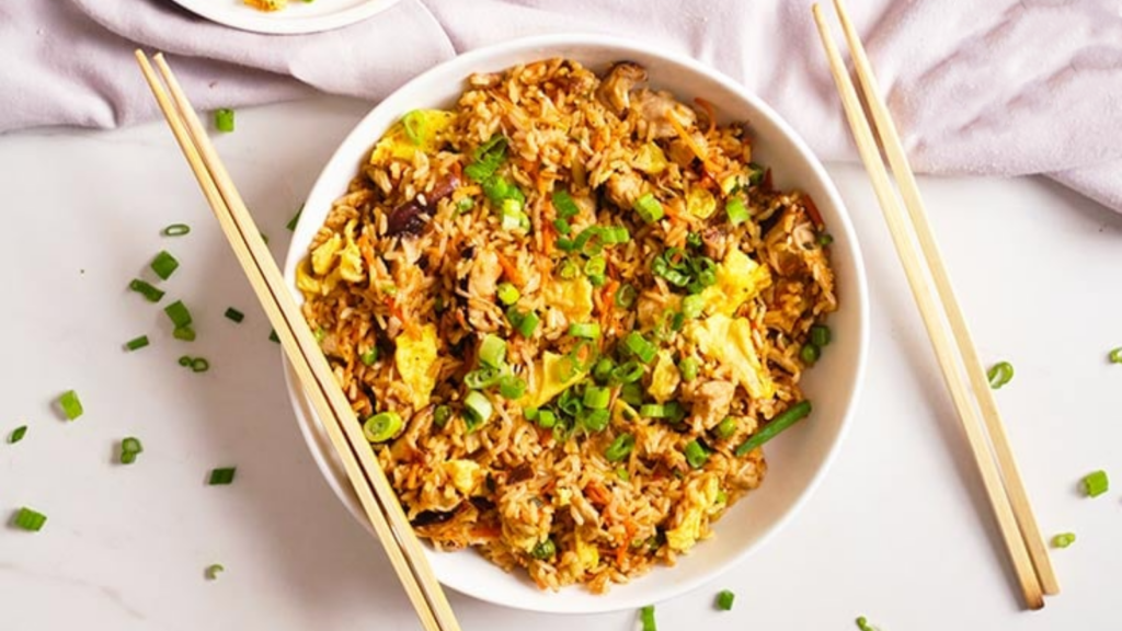 An overhead view of a white bowl filled with pork fried rice. Two sets of chopsticks lay on and by the bowl.