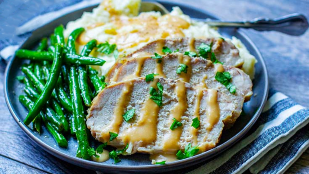A blue plate holds three slices of pork loin with drizzles of gravy, some green beans and mashed potatoes with gravy.