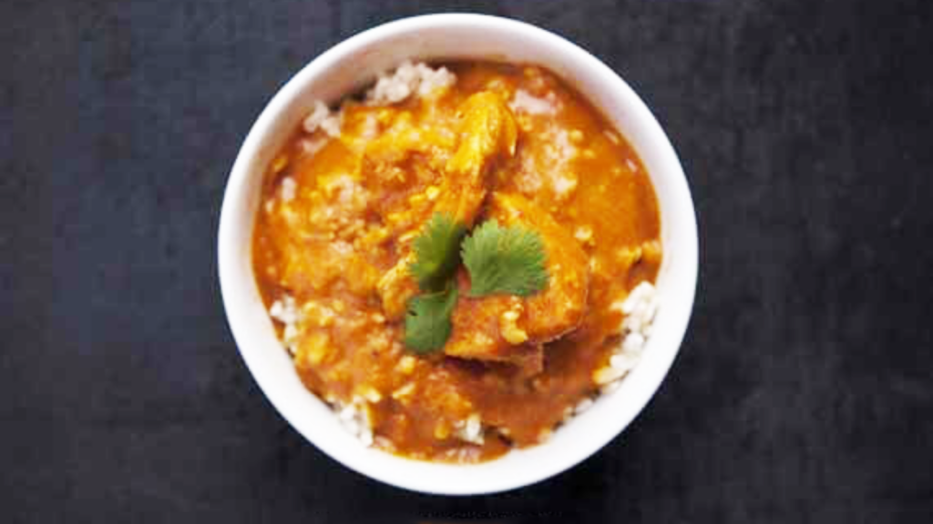 An overhead view of a white bowl filled with pumpkin chicken curry.