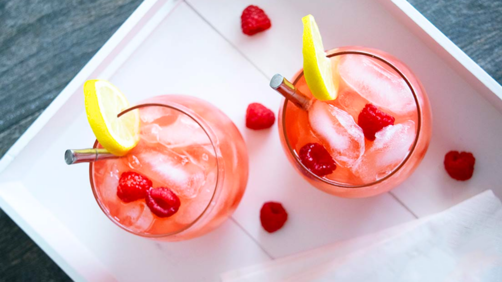 An overhead view of two glassed on a white tray filled with raspberry lemonade and garnished with fresh raspberries and lemon slices.