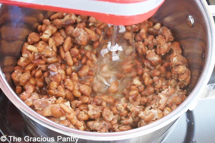 Mashing the beans and water in a pot to make refried beans.