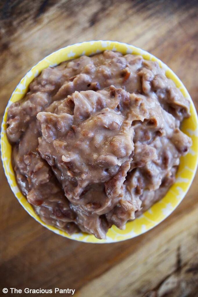 An overhead view looking down into a yellow bowl filled with healthy refried beans.