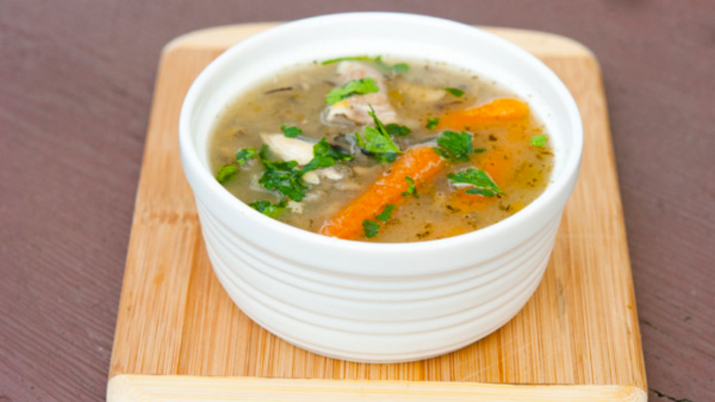 A white bowl sits on a cutting board filled with rotisserie chicken soup.