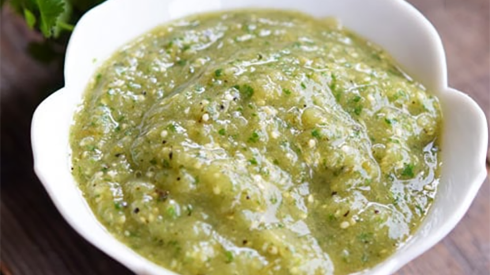 A closeup of a white, fluted bowl filled with salsa verde sauce.