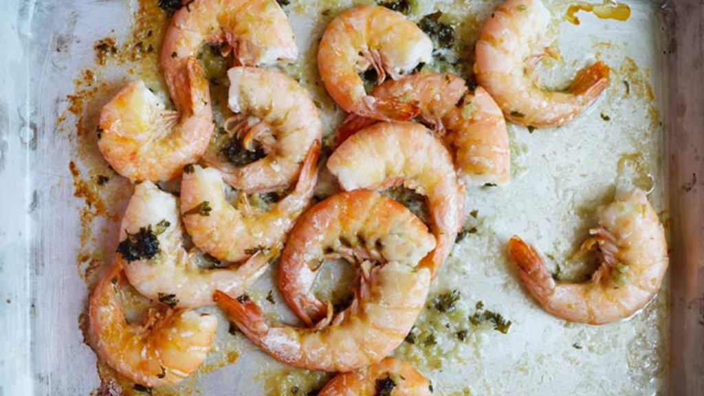 Sheet pan garlic shrimp laying on a baking pan smothered in butter and parsley.