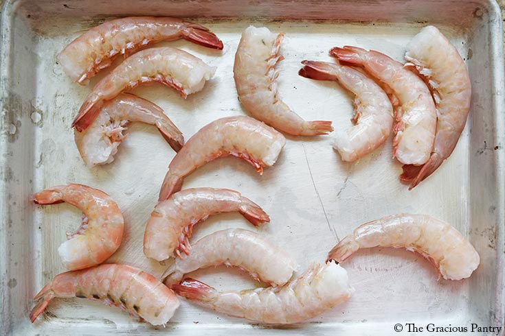 Raw shrimp in shells laying on a sheet pan.