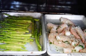 Two sheet pans in an oven. One holds asparagus, the other holds Sheet pan garlic butter shrimp.