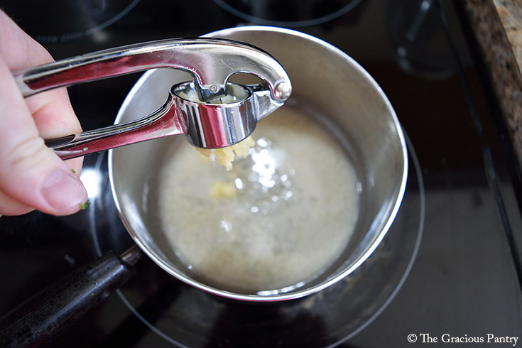 Adding pressed garlic to melting butter in a pot.