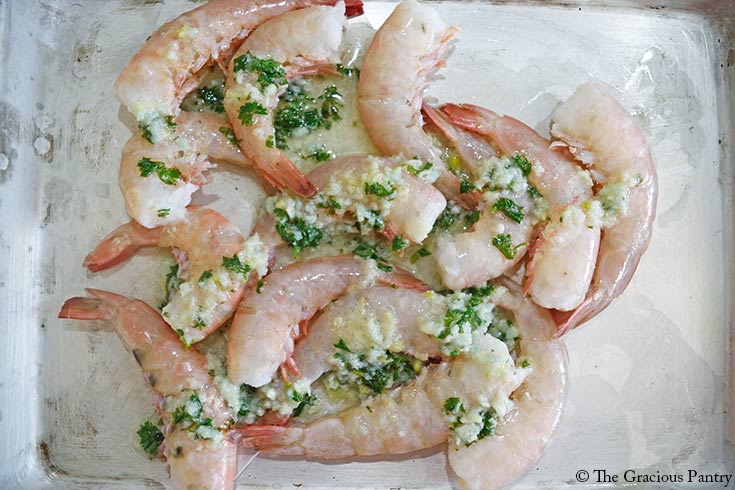 Garlic butter poured over raw shrimp on a sheet pan.