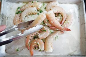 Tossing shrimp in garlic butter sauce using tongs on a sheet pan.