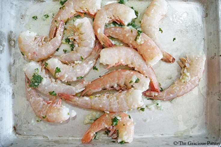 Seasoned garlic butter shrimp laying on a sheet pan.