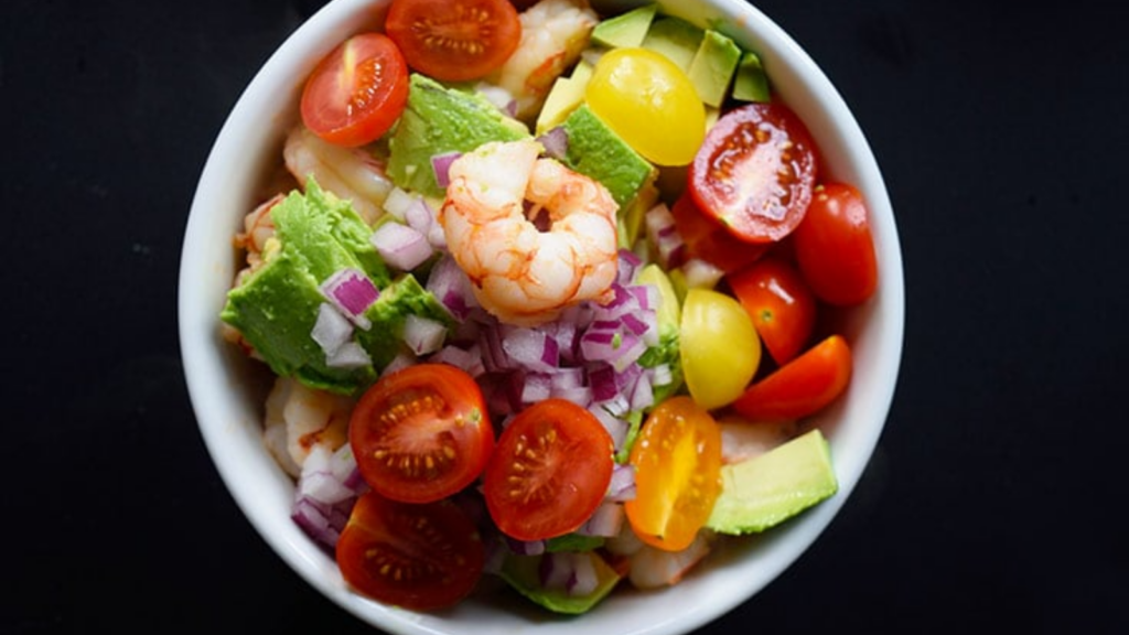 An overhead view of a white bowl filled with shrimp and avocado salad.