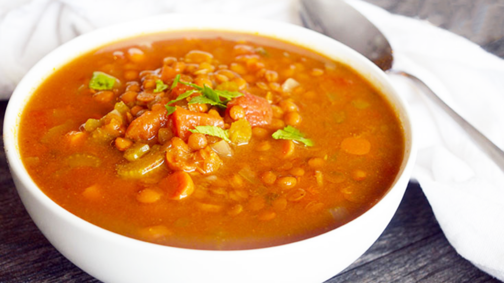 A white bowl filled with slow cooker curry lentil soup sits on a gray surface.