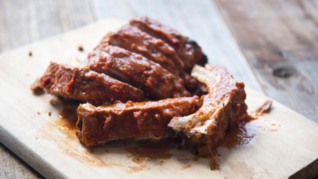 A pile of baby back ribs on a wooden cutting board.