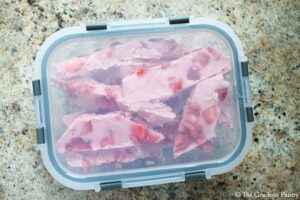 Strawberry Frozen Yogurt Bark pieces packed into a freezer-safe container to store in the freezer.