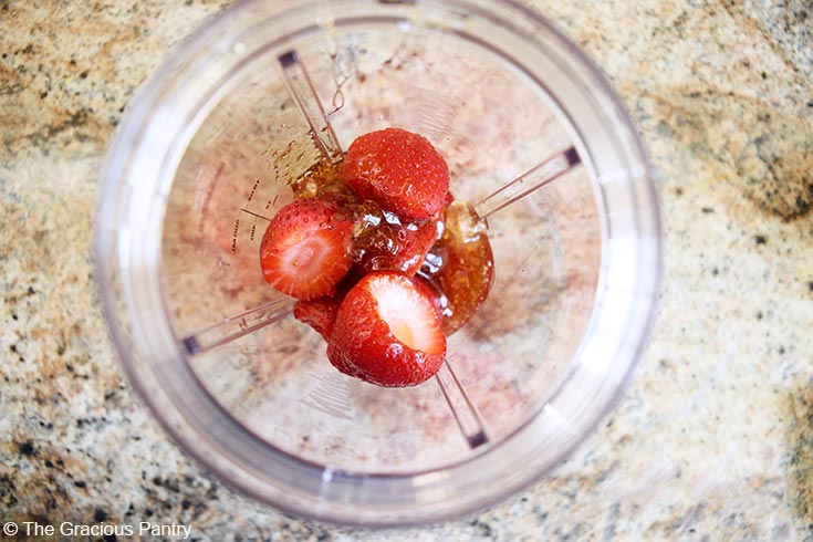 Sweetener and strawberries in a blender tumbler.