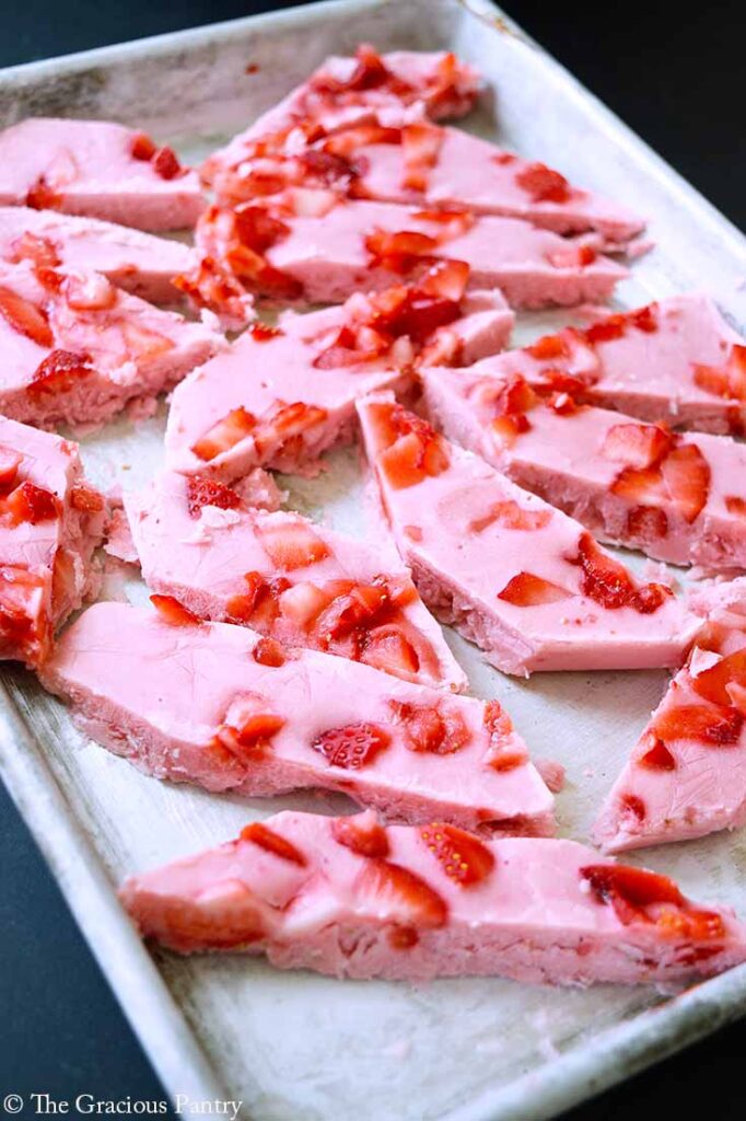 A side view of a baking sheet covered in pieces of Strawberry Frozen Yogurt Bark.