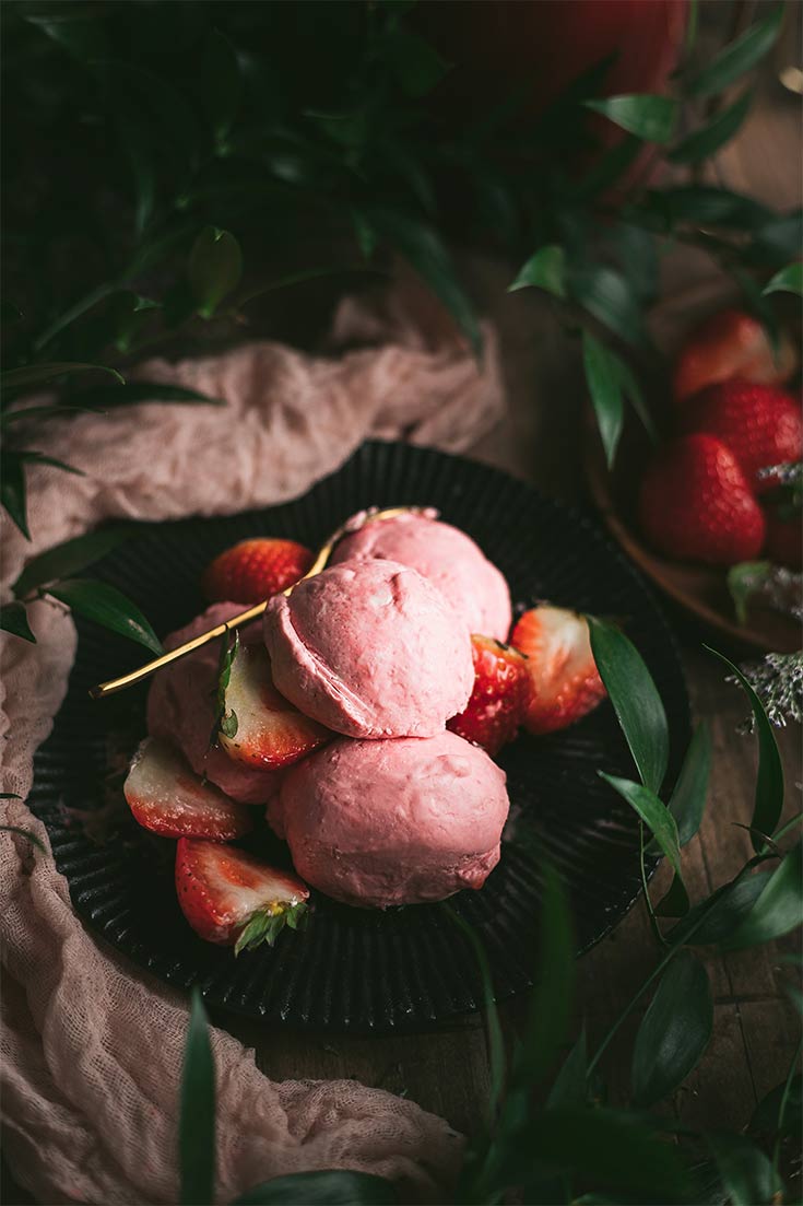 Three scoops of Strawberry Nice Cream sit on a pile of fresh strawberries on a black plate.