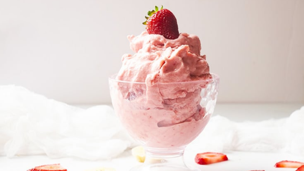 Strawberry nice cream piled high in a glass ice cream bowl and topped with a fresh strawberry.