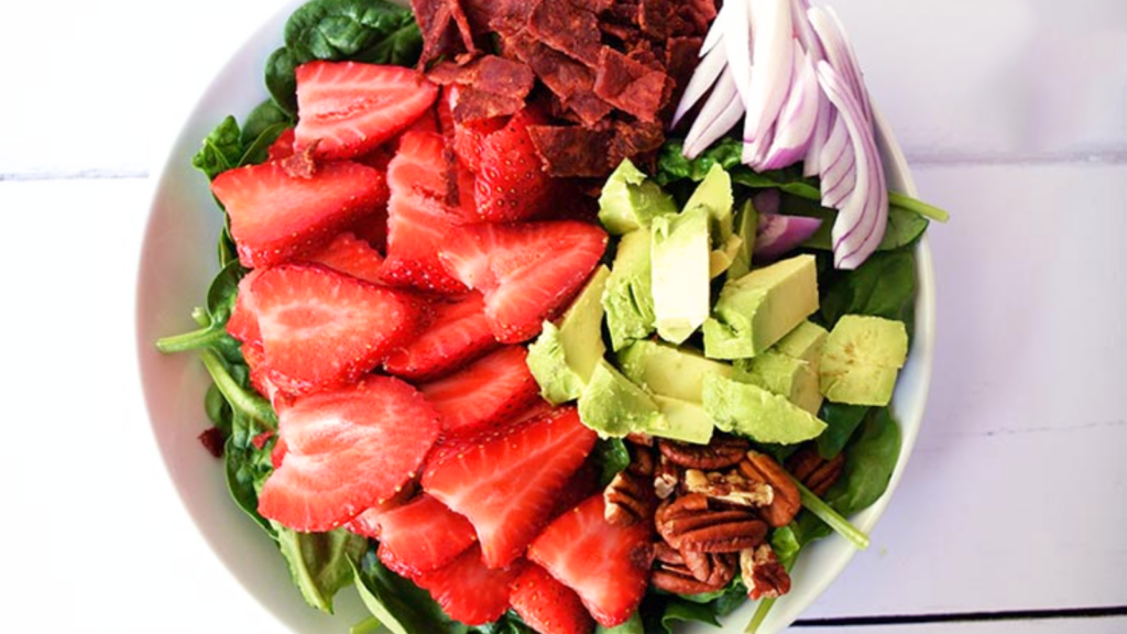 An overhead view of a strawberry spinach salad in a white bowl.
