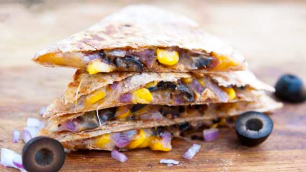 Stacked stuffed Mexican quesadilla pieces on a cutting board with a few black olives laying around the stack.