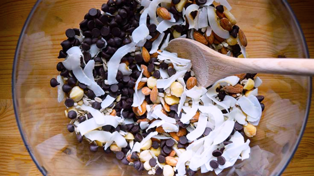 An overhead view of a glass bowl filled with low carb trail mix. A wooden spoon rests in the bowl.