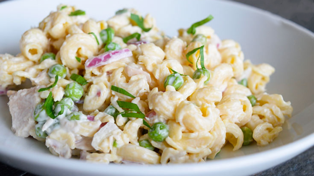 A white bowl holds a serving of tuna pasta salad and is garnished with fresh greens.