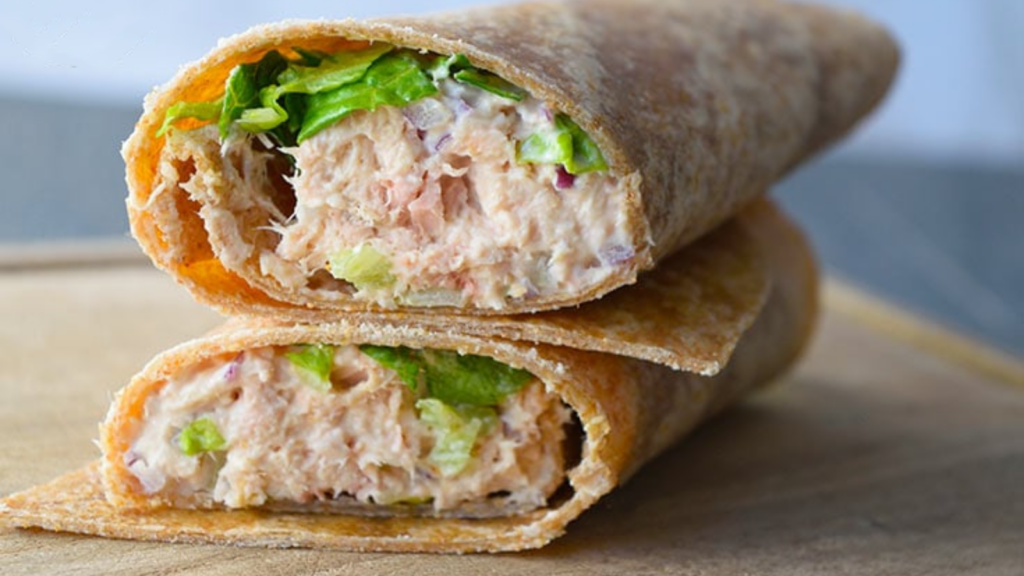 A tuna wrap lays cut in half and stacked so you can see the tuna and lettuce inside.