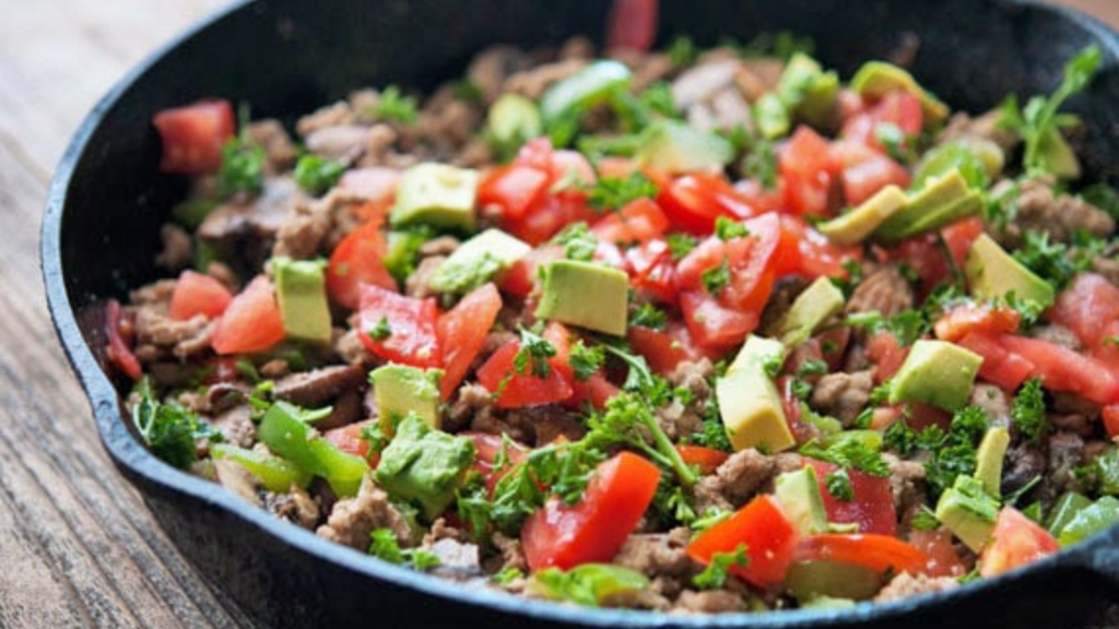 A skillet filled with ground turkey, chopped tomatoes, chopped avocado and garnished with fresh parsley.
