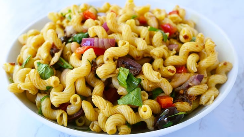 A side view of a white bowl filled with Tuscan pasta salad.