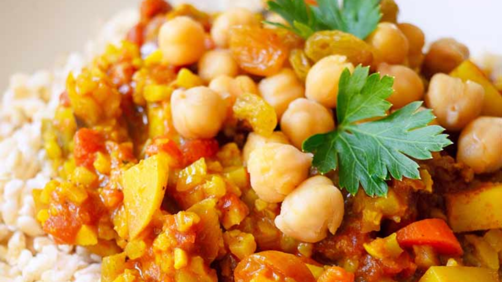 A closeup of vegetable curry with chickpeas and golden raisins on top.