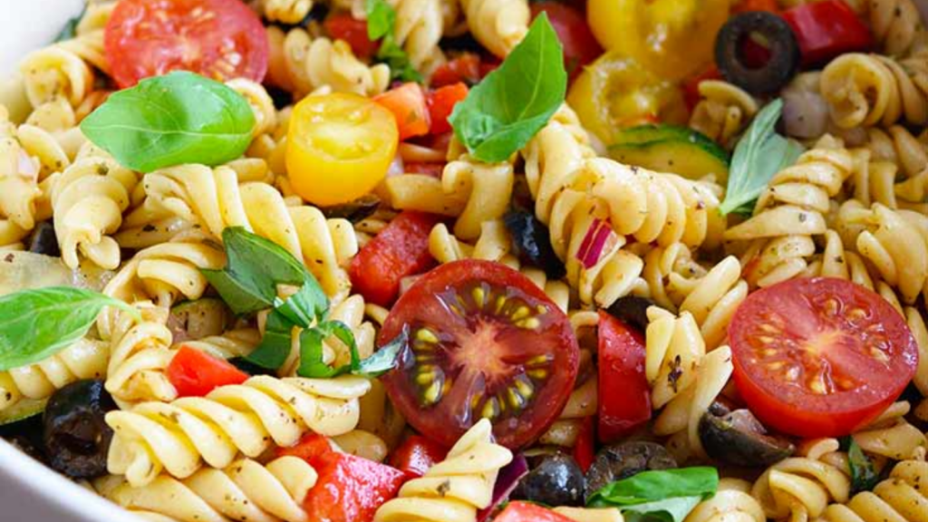 A closeup of a white bowl filled with vegetable pasta salad.