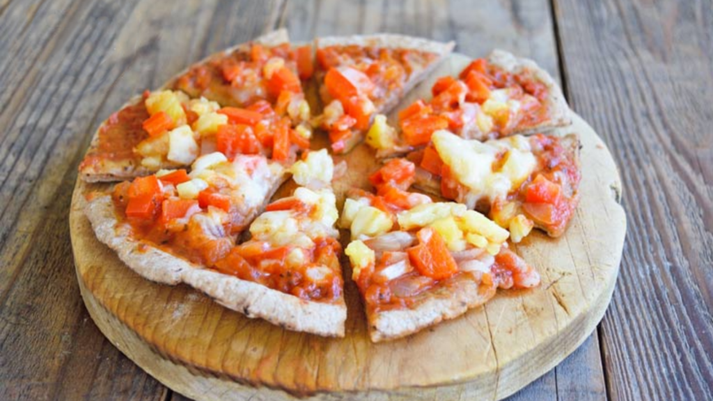 A vegetarian pita pizza sits on a round cutting board on a wood table.