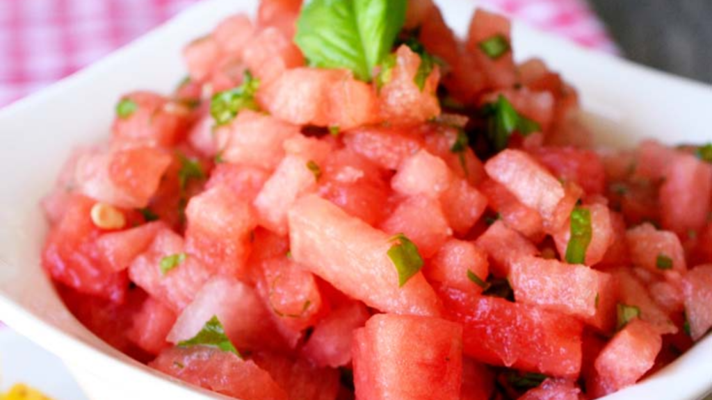 A closeup of a white bowl filled with watermelon salsa which is garnished with fresh basil.