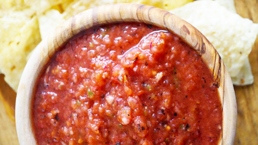 An overhead view of a wood bowl filled with red salsa and corn chips behind it.