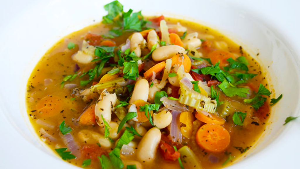 A white bowl sits filled with white bean soup.