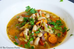 A white bowl filled with white bean soup and garnished with fresh, chopped parsley.