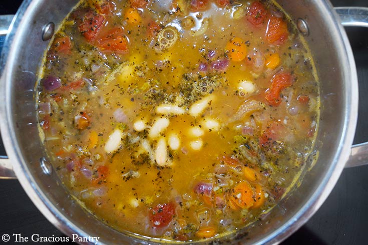 White beans added to broth and veggies cooking in a pot.