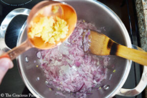 Adding pressed garlic to sautéing onions.