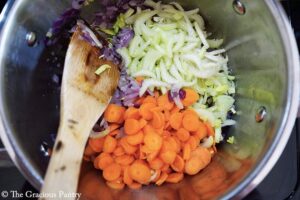 Celery and carrots added to a pot of sautéing onions.