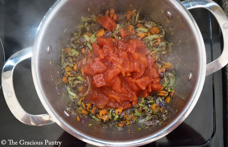 Diced tomatoes added to a pot of cooking veggies.