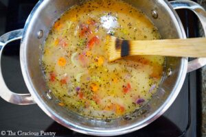 Broth added to a pot of cooking veggies.