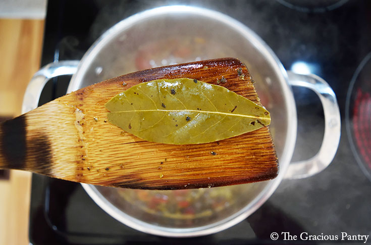 A bay leaf being removed from a pot of white bean soup after cooking.