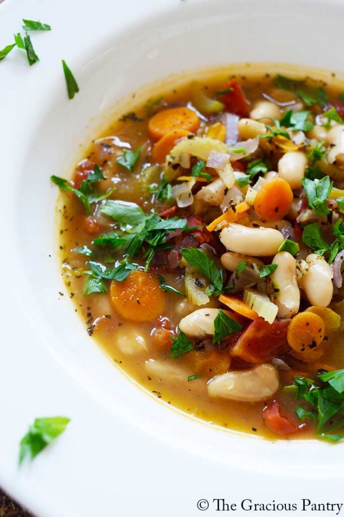 A wide-rimmed, white bowl holds a serving of white bean soup that has been garnished with fresh parsley.