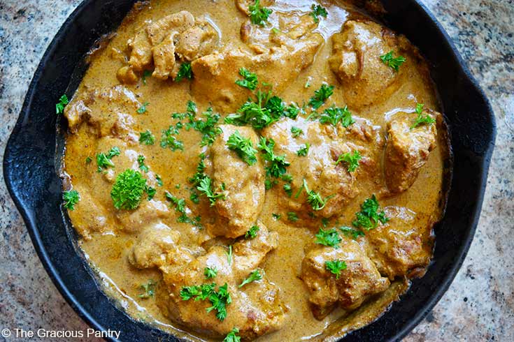 A cast iron skillet holds a full pan of just-baked Yogurt Chicken. It is garnished with chopped parsley.