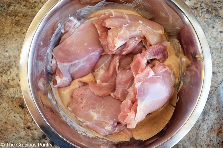 Chicken added to yogurt sauce in a mixing bowl.