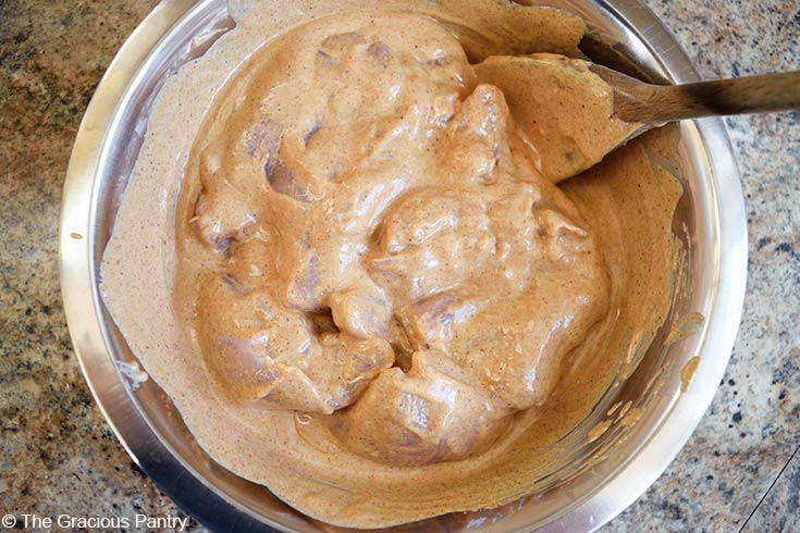 Chicken mixed into yogurt sauce in a mixing bowl.