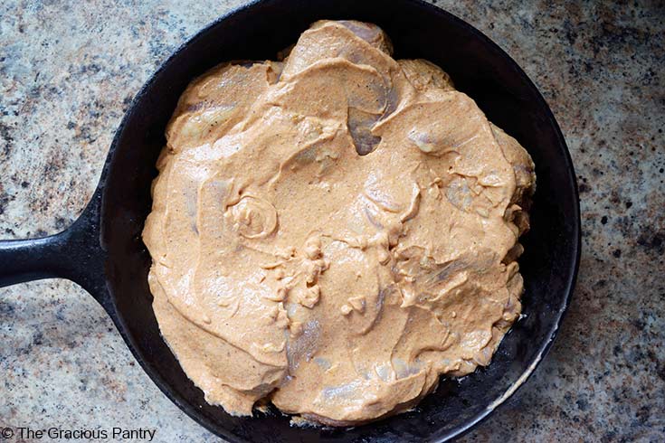 Yogurt chicken sitting in a cast iron skillet with yogurt sauce evenly spread over the top of the raw chicken.